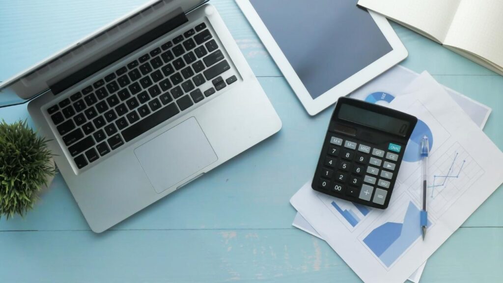 mesa com notebook, tablet, calculadora e gráficos financeiros.