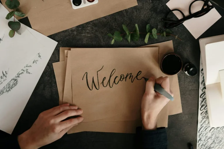 Pessoa escrevendo "welcome" em papel cartão pardo