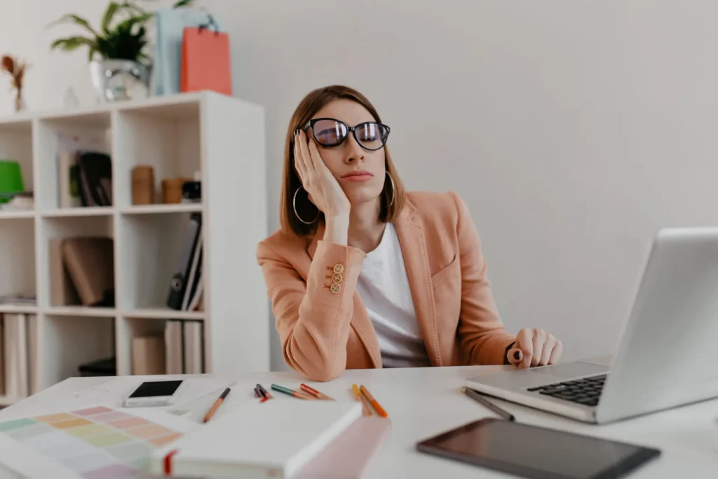 Mulher usando óculos cansada caindo no sono em mesa de trabalho com seu notebook