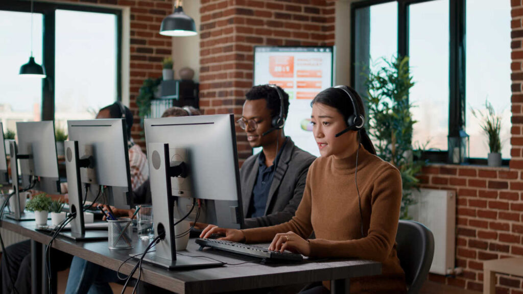 Agentes de atendimento ao cliente em um call center, usando fones de ouvido e trabalhando em computadores.