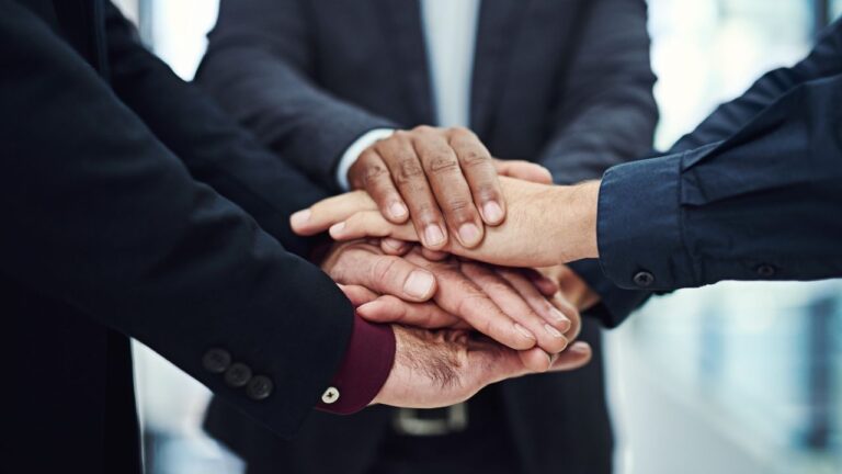 pessoas de terno juntando as mãos no centro em grupo.