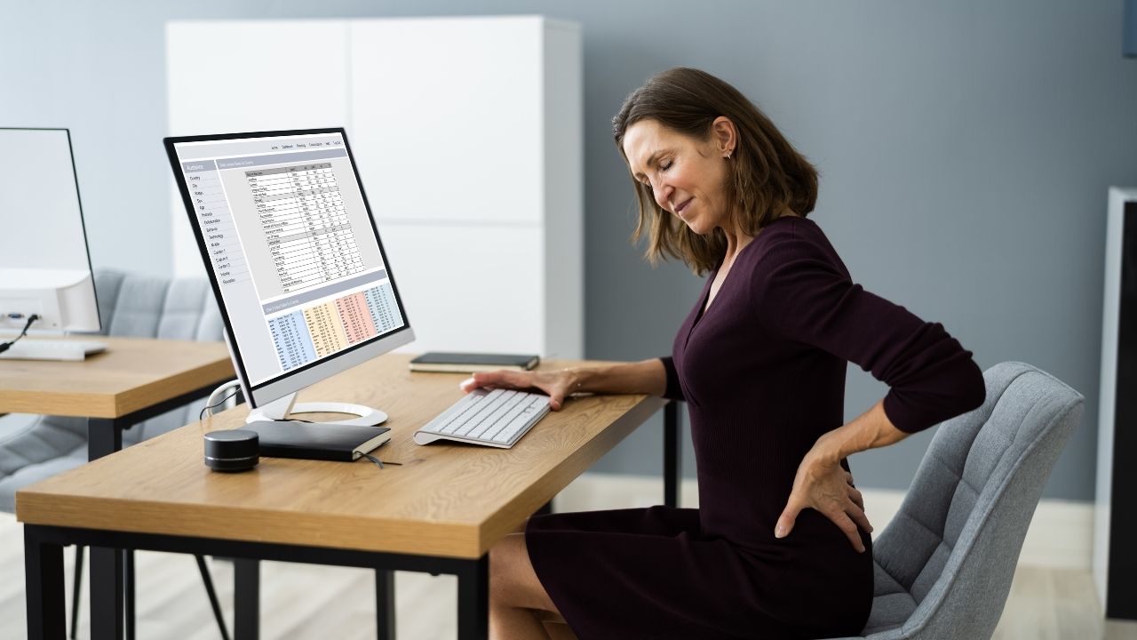 mulher com dor nas costas sentada em frente ao computador no escritório.