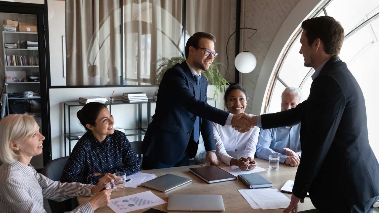 reunião de equipe com profissionais sorrindo e dois executivos apertando as mãos.